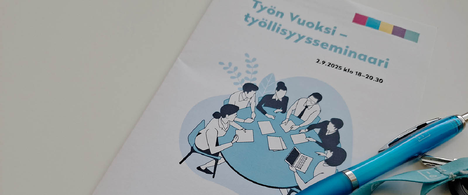 Seminaariohjelma, jonka päällä turkoosi kuulakärkikynä ja avainnauha.
