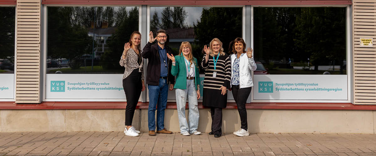 Suupohjan työllisyysalueen työntekijät seisovat toimiston ulko-oven vieressä rivissä hymyillen ja heiluttavat.
